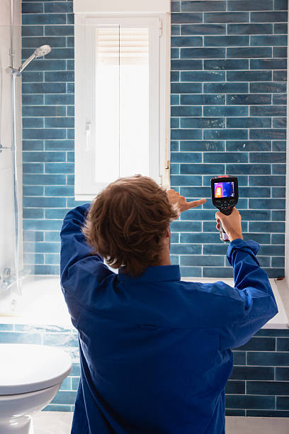 man in blue uniform inspecting a bathroom wall with a thermal imaging camera